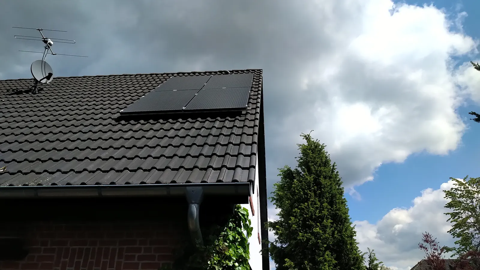 Schwarze Solarmodule auf einem dunklen Ziegeldach unter Wolkenhimmel